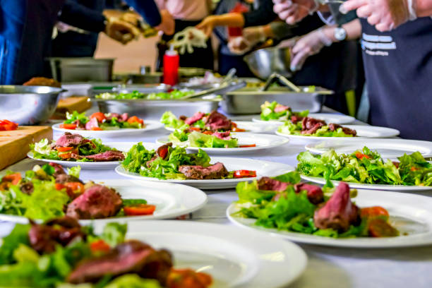 cooked roast beef, fresh salad and tomatoes served on white plates. cooking master class, workshop with people learning how to cook around the table - commercial kitchen restaurant chef food service occupation imagens e fotografias de stock
