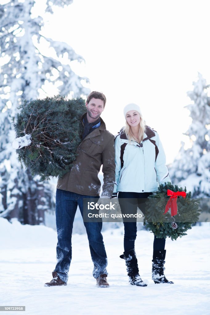 Adorable jeune Couple transportant couronne et arbre de Noël dans la neige - Photo de Jeune couple libre de droits