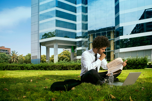 Businessman reading the newspaper outdoors, in front of a corporate building.