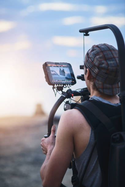 Look at that view Over the shoulder shot of a focused young man shooting a scene with a state of the art video camera outside on a beach during the day film crew photos stock pictures, royalty-free photos & images