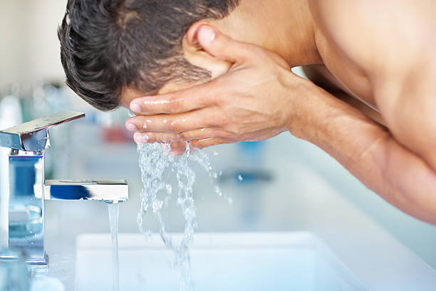 giovane ragazzo pulizia viso con acqua nel lavandino - lavarsi il viso foto e immagini stock