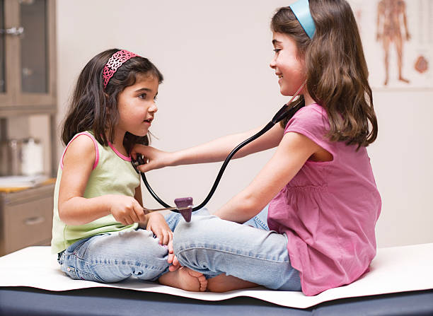Two little girls in doctors office sitting on exam table in clinic facing each playing doctor.    Girl in pink shirt is using stethoscope and girl in green shirt is using a reflex hammer.  Stainless steel medical cabinet with supplies in background.  Medical poster on wall. Horizontal shot.\n\nExclusive only at istockphoto. Steve Cole Images, Atlanta, Ga\n• Exclusive image links listed below by subject. •\n\n[url=http://www.istockphoto.com/file_search.php?action=file&lightboxID=9102587\n[img]http://dl.dropbox.com/u/40249541/ISP%20Banners/BabyHealthcare.jpg[/img][/url]\n[url=http://www.istockphoto.com/search/lightbox/12422807#8be6e0f\n[img]http://dl.dropbox.com/u/40249541/ISP%20Banners/Pharmacy.jpg[/img][/url]\n[url=http://www.istockphoto.com/file_search.php?action=file&lightboxID=5685663\n[img]http://dl.dropbox.com/u/40249541/ISP%20Banners/Healthcare.jpg[/img][/url]\n[url=http://www.istockphoto.com/file_search.php?action=file&lightboxID=8589366\n[img]http://dl.dropbox.com/u/40249541/ISP%20Banners/SeniorHealthcare.jpg[/img][/url]