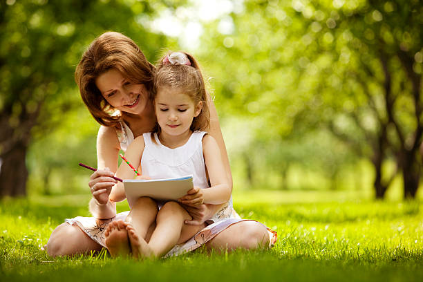 Smiling woman and a girl sitting on the grass drawing stock photo