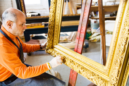 An artist doing restoration to an antique gold picture frame.