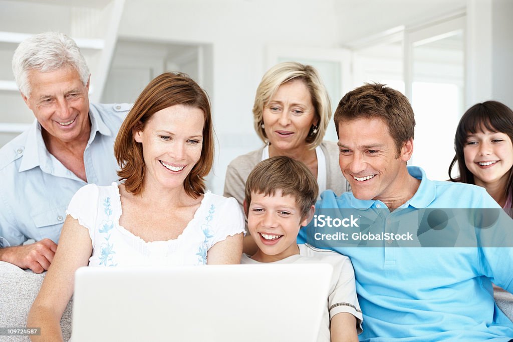 Familia sentada en el sofá usando una computadora portátil en la sala de estar - Foto de stock de Familia libre de derechos