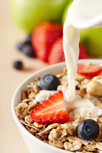 Spoon with corn flakes with a bowl full with corn flakes in the background. Focus is on the spoon.
