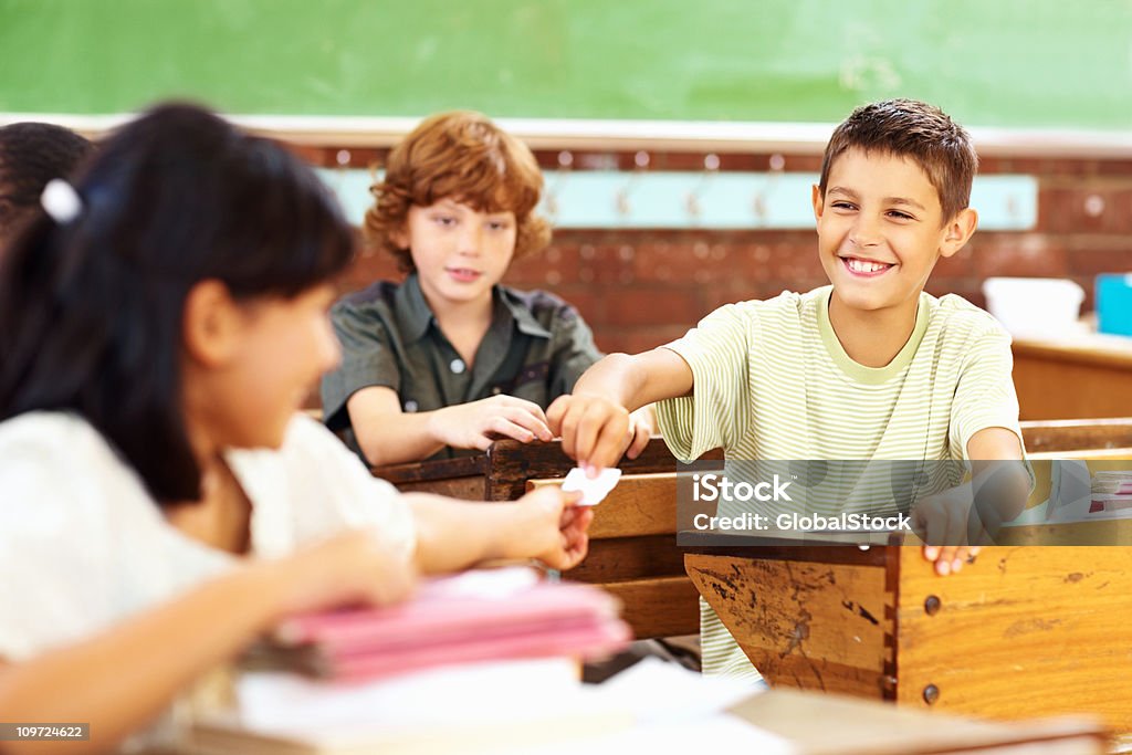 Feliz school boy de pasar a un papel classmate - Foto de stock de Travesura libre de derechos