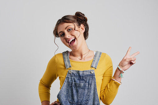 Studio shot of an attractive young woman making a peace sign against a grey background