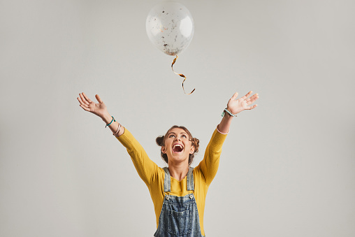 Studio shot of an attractive young woman playing with a balloon against a grey background