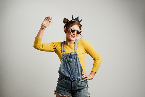Studio shot of an attractive young woman wearing sunglasses and a crown against a grey background