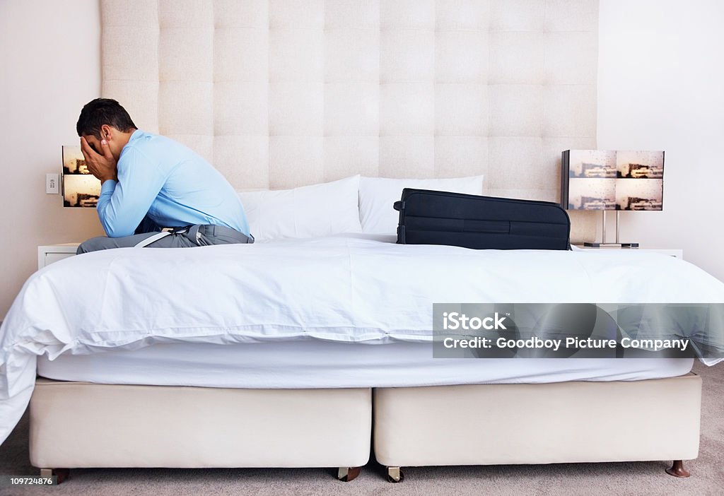 Joven empresario sentado en el dormitorio con rostro cubierto - Foto de stock de 20 a 29 años libre de derechos