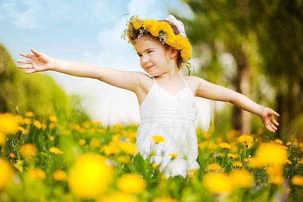 Little girl standing among dandelions with arms outstretched stock photo
