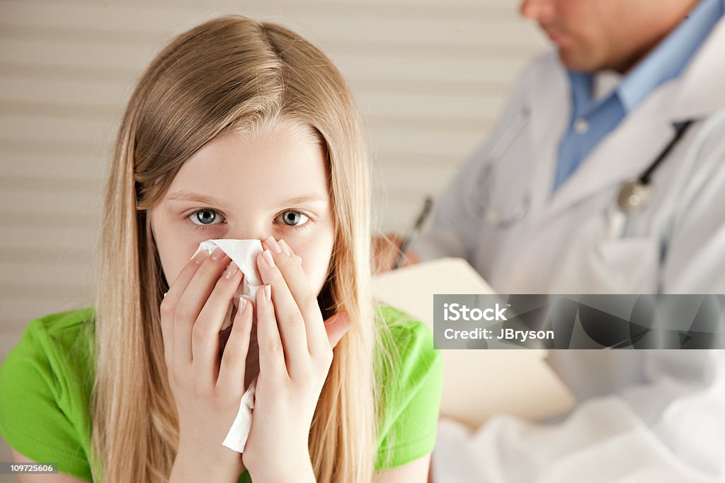 Sick Little Girl Blowing Her Nose in the Doctors Office  10-11 Years Stock Photo