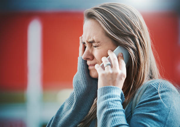 Young woman gets bad news on her mobile phone A young blonde woman grimaces, hand to her face as she hears something on her smart phone, obviously bad news. cheek cell stock pictures, royalty-free photos & images