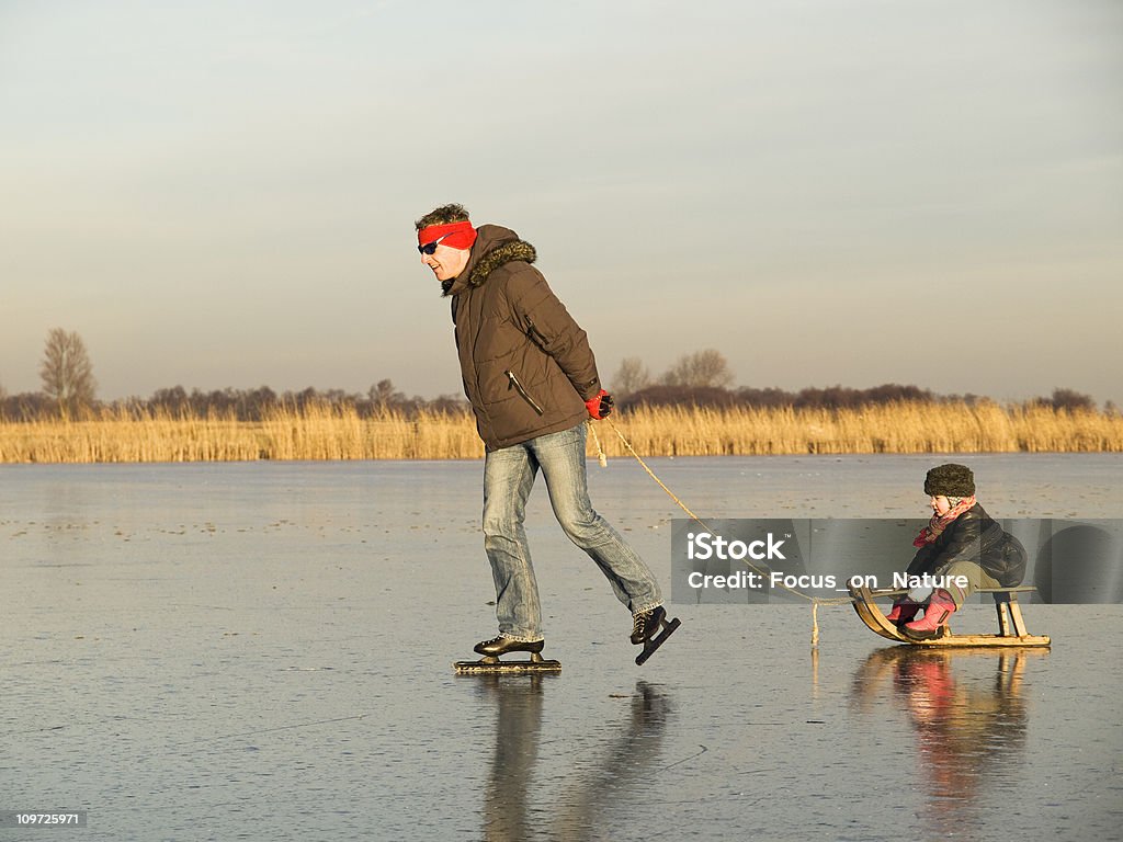 Pattinaggio su ghiaccio di uomo tirando figlio sulla slitta - Foto stock royalty-free di Canale