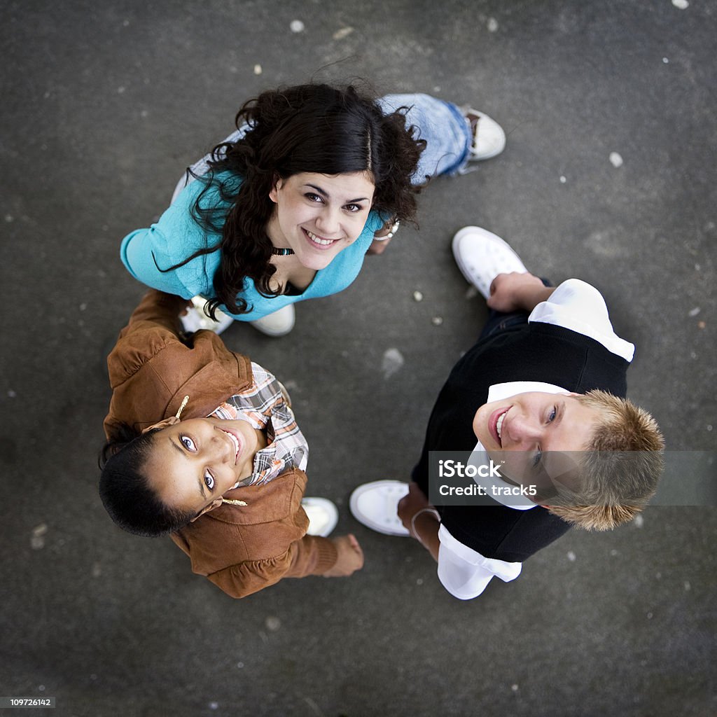 three friends standing in a circle looking up and smiling  Three People Stock Photo