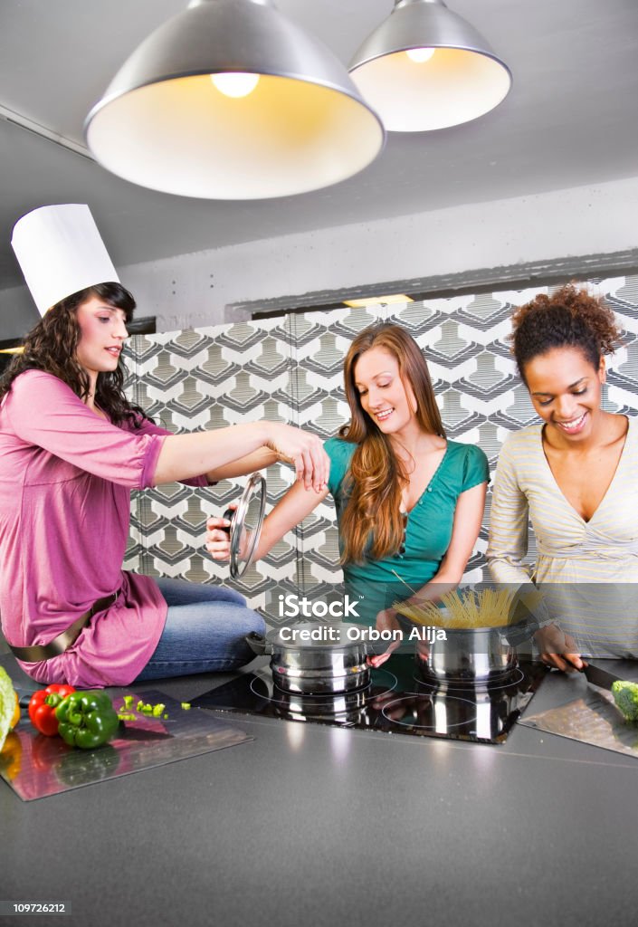 Three Young Women Preparing Dinner Around Stove  Adult Stock Photo