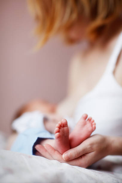 Woman nursing a tiny newborn baby and holding his feet stock photo