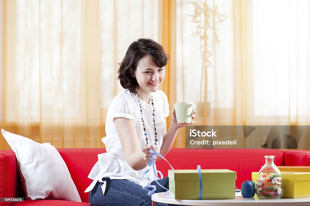 Jeune femme assise sur un canapé et arranger des cadeaux - Photo de 25-29 ans libre de droits