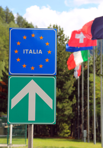 road sign of the Italian border direction with flags on the background