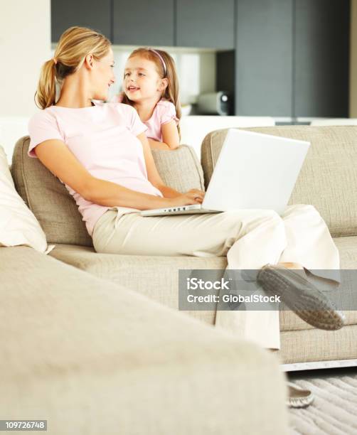 Young Woman Working On Laptop With Daughter Standing Beside Her Stock Photo - Download Image Now