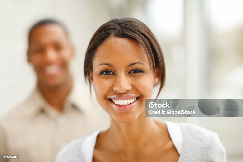 Jovem mulher sorridente com homem no fundo - Foto de stock de 20 Anos royalty-free