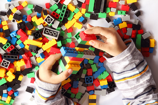 Close up of child's hand playing plastic toy building blocks, top view from above.