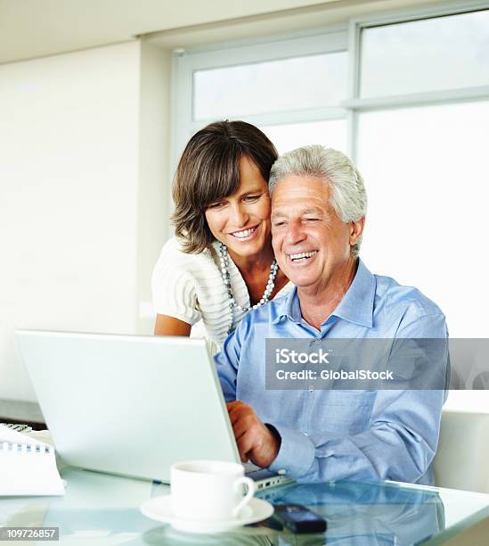 Foto de Casal Maduro Usando O Laptop Em Casa E Sorrindo e mais fotos de stock de 50-54 anos - 50-54 anos, Casa, Casal de Meia Idade