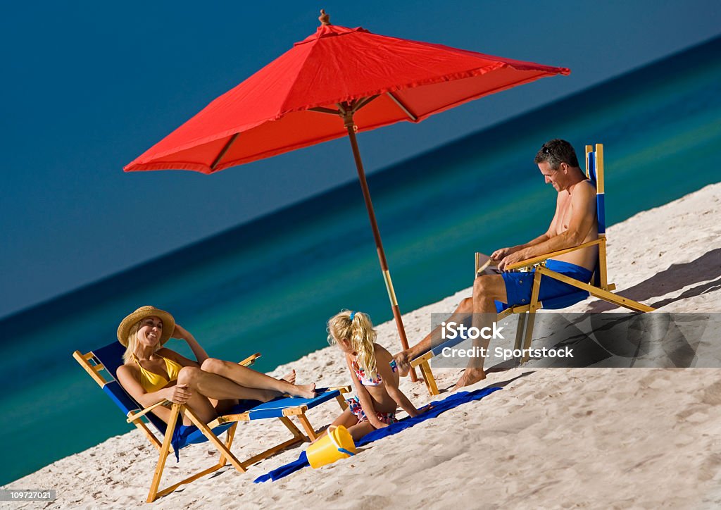 Familie sitzend unter Sonnenschirm am Strand - Lizenzfrei Badebekleidung Stock-Foto
