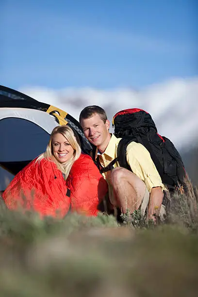 Close-up of young couple sitting in front of tent smiling and looking at the camera.