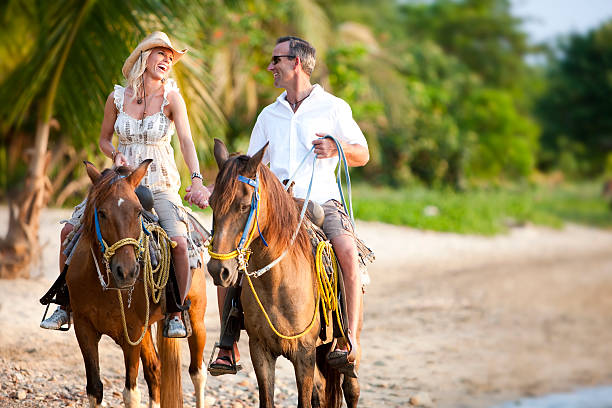 Vacation Lifestyles-Couple Riding Horses on Beach at Sunset stock photo
