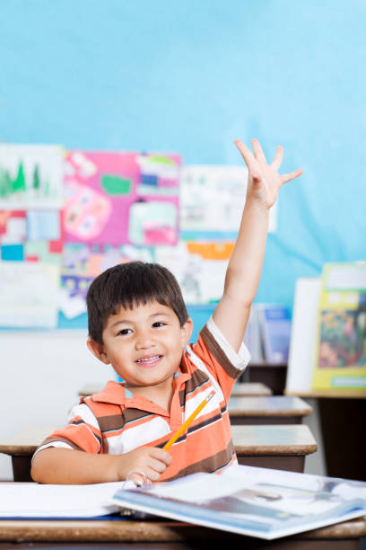восхитительный милый мальчик поднимая руки в начальной школы классная комната - asian ethnicity child little boys education стоковые фото и изображения