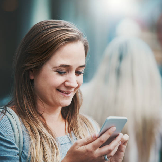 istock Smiling woman looks down, standing in street sending text message 1097291818
