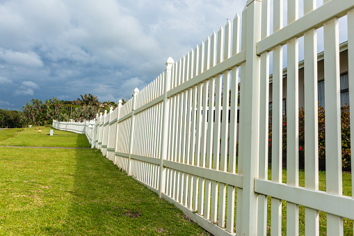 White boundary vertical slat plastic pvc fence wall along roadside grass landscape.