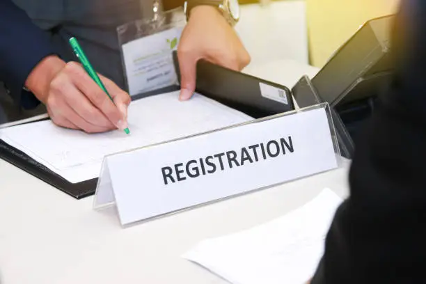 Photo of close-up of registration desk in front of conference center with Businessman Writing on the Table