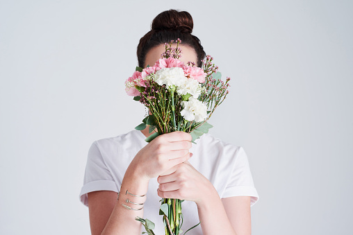 Studio shot of an unrecognizable woman covering her face with flowers against a grey background