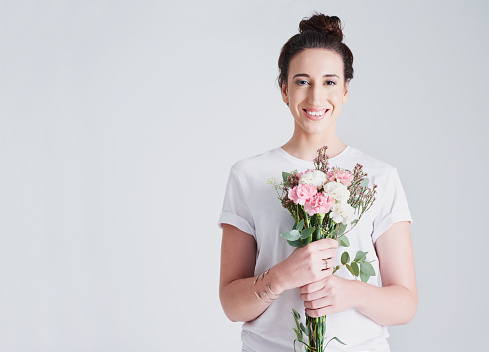 Studio shot of a beautiful young woman holding a bouquet of flowers against a grey background