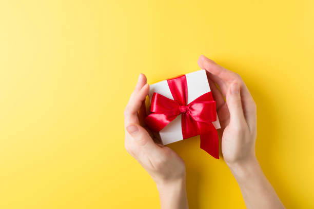 istock Womman's hand holding a gift box over yellow background, valentines theme 1097310474