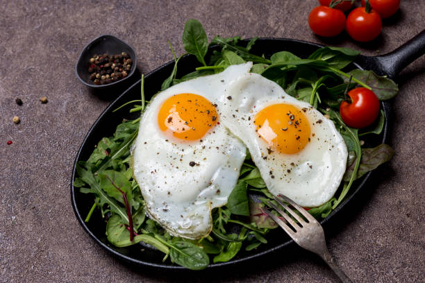 istock Fried eggs sunny side up on pan with herbs, cherry tomatoes and pepper, with fork an brown background. Concept of healthy breakfast 1097310910