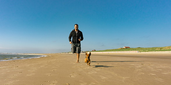Man with his little cute dog running at the beach