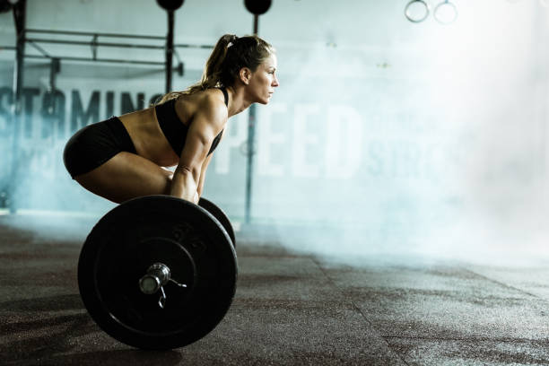 Side view of athletic woman exercising deadlift in a gym. Muscular build woman exercising deadlift with barbell in a health club. Copy space. squatting position photos stock pictures, royalty-free photos & images