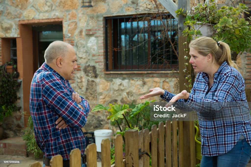 Woman quarreling with male neighbor Angry woman quarreling with her male neighbor, talking through wooden fence Neighbor Stock Photo