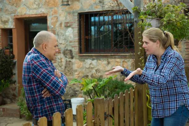 Angry woman quarreling with her male neighbor, talking through wooden fence