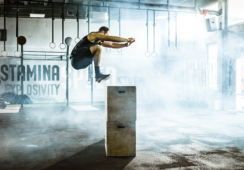 Athletic man jumping on a crate while having sports training in a gym.