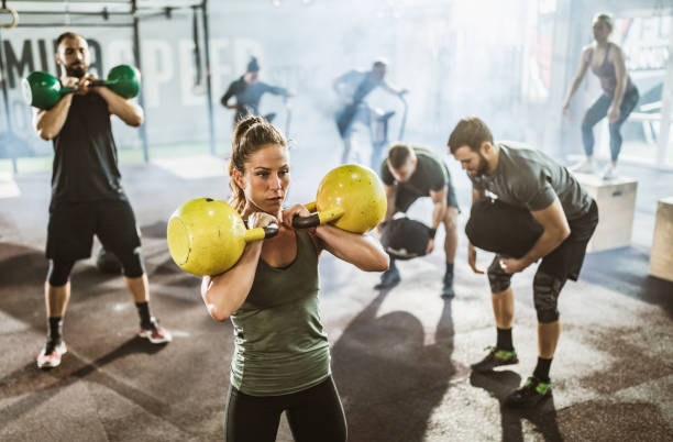 Large group of athletes exercising strength of cross training in a gym. Large group of athletic people having sport training in a gym. Focus is on woman with kettle bells. circuit training stock pictures, royalty-free photos & images