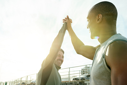Shot of two sporty men giving each other a high five while exercising outdoors
