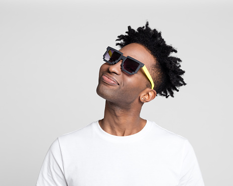 Portrait of handsome afro american man in white t-shirt wearing funky sunglasses looking away against gray background.