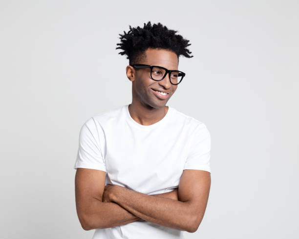 Happy afro american man with nerd eyeglasses looking away Portrait of happy afro american guy with nerd eyeglasses. Man wearing white t-shirt looking away with arms crossed. black nerd stock pictures, royalty-free photos & images