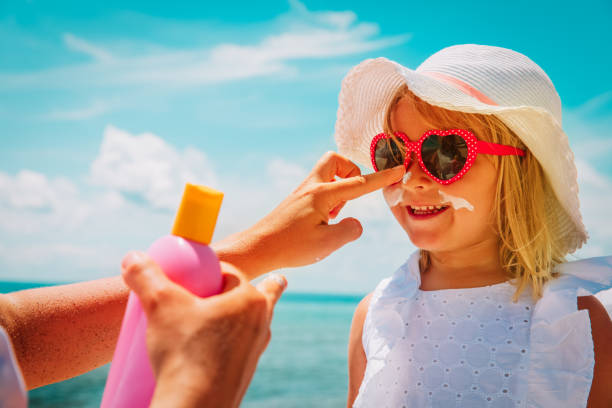mother put sunblock cream on little daughter face at beach - child beach playing sun imagens e fotografias de stock