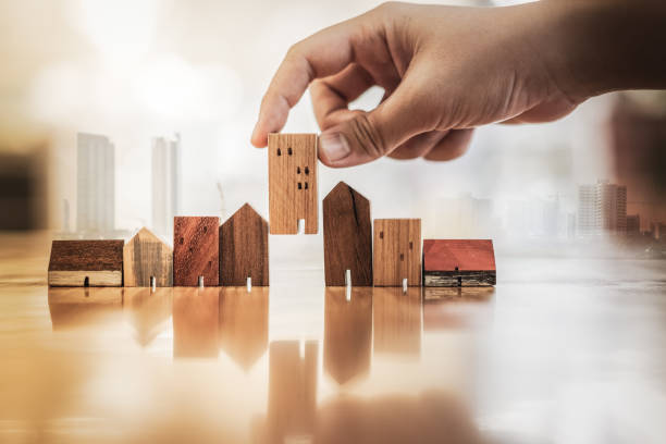 istock Hand choosing mini wood house model from model on wood table, selective focus, Planning to buy property. Choose what's the best. A symbol for construction ,ecology, loan concepts 1097336480